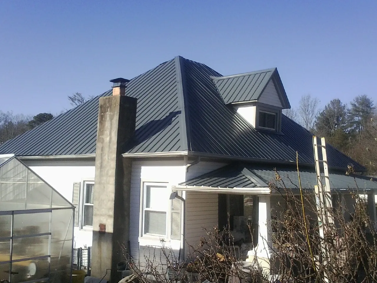 Dark blue standing seam metal roof on a white farmhouse with dormer — Slate & Tile Roof Repair by Roofing Brothers in Livingston