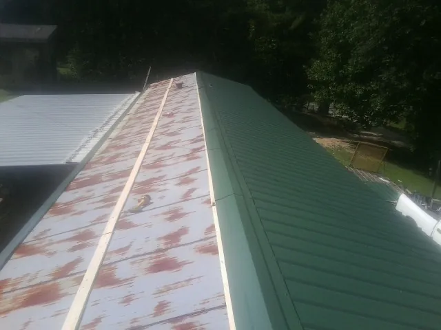 Old rusted panels beside newly installed green metal roofing — Wind Damage Roof Repair by Roofing Brothers in Livingston