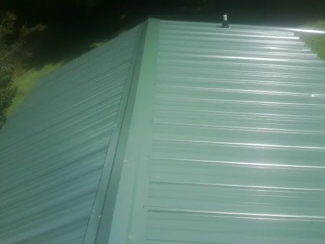 New green metal panels meeting at the ridge of a roof — Flat Roof Repair work by our crew in Livingston